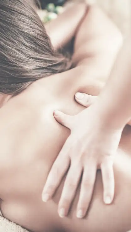 Primer plano de manos femeninas realizando un masaje descontracturante en la parte superior de la espalda de una mujer